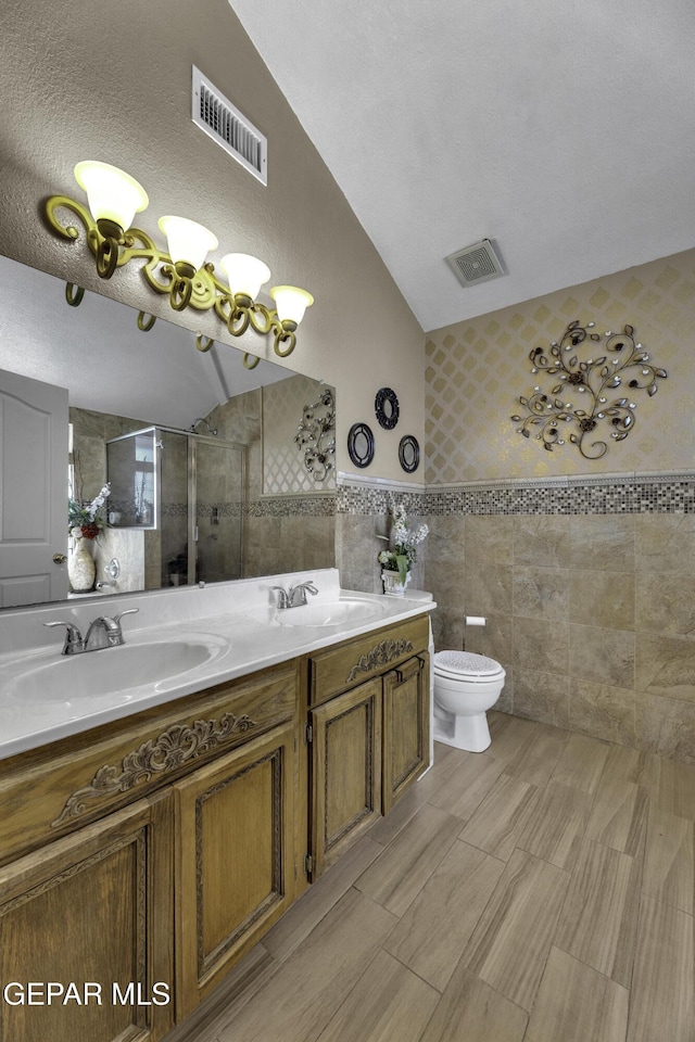 bathroom with toilet, a shower with shower door, vaulted ceiling, tile walls, and vanity