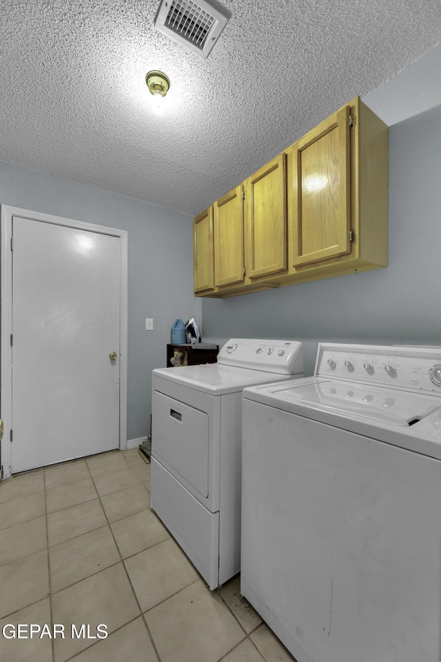 laundry room featuring cabinets, washer and dryer, light tile patterned floors, and a textured ceiling