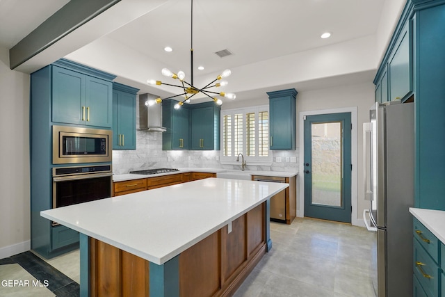 kitchen with wall chimney exhaust hood, appliances with stainless steel finishes, blue cabinetry, and a kitchen island