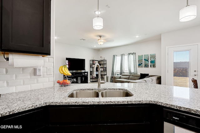 kitchen with decorative light fixtures, sink, dishwashing machine, backsplash, and light stone countertops