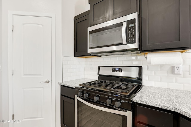 kitchen featuring dark brown cabinetry, appliances with stainless steel finishes, light stone countertops, and backsplash