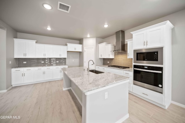 kitchen with wall chimney exhaust hood, sink, a center island with sink, stainless steel appliances, and white cabinets