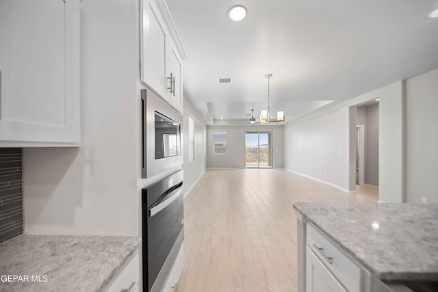 kitchen with light stone countertops, stainless steel microwave, white cabinets, and black oven