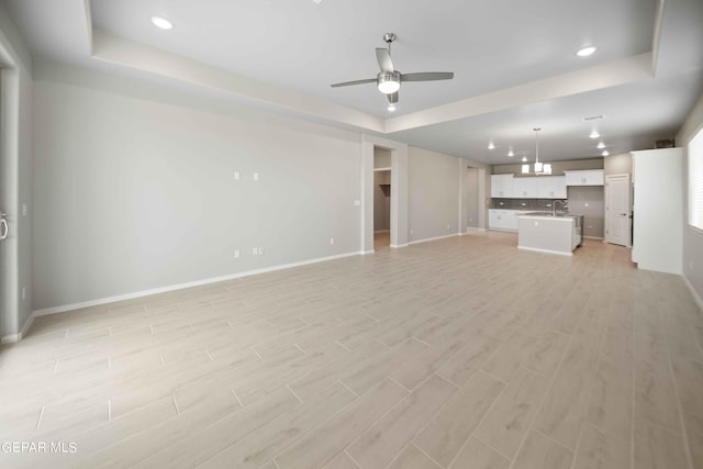 unfurnished living room featuring a tray ceiling, light hardwood / wood-style flooring, and ceiling fan