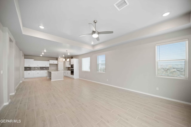 unfurnished living room with sink, a tray ceiling, ceiling fan, and light wood-type flooring