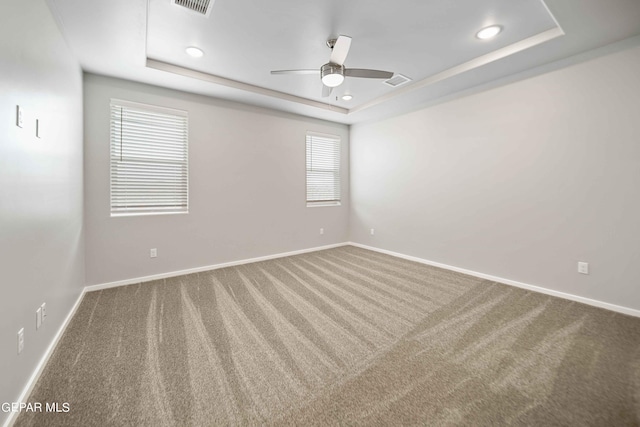 empty room with a raised ceiling, carpet, and ceiling fan