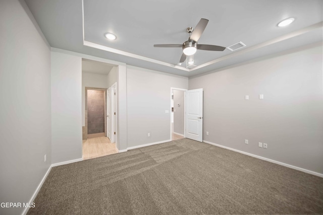 unfurnished bedroom with ensuite bathroom, carpet, ceiling fan, and a tray ceiling