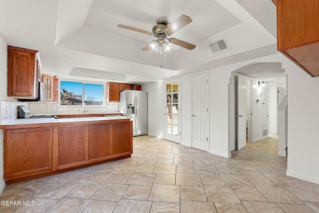 kitchen with ceiling fan, appliances with stainless steel finishes, tasteful backsplash, kitchen peninsula, and a raised ceiling