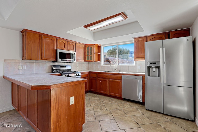 kitchen with appliances with stainless steel finishes, tile countertops, tasteful backsplash, sink, and kitchen peninsula