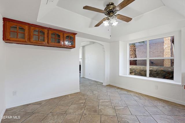 empty room with ceiling fan and a raised ceiling