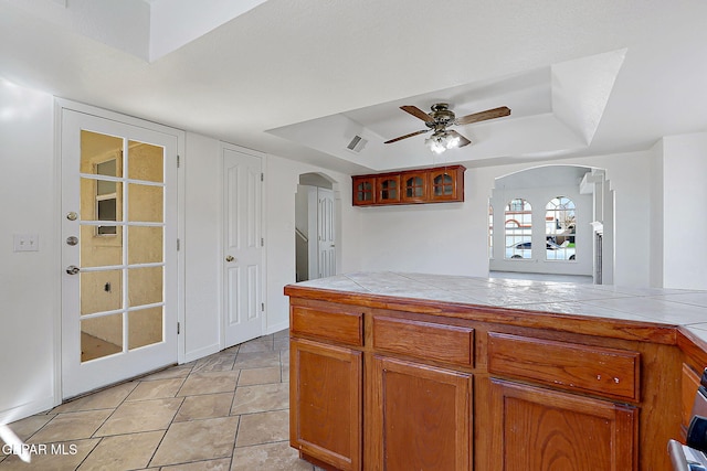 kitchen featuring ceiling fan, a tray ceiling, and tile counters