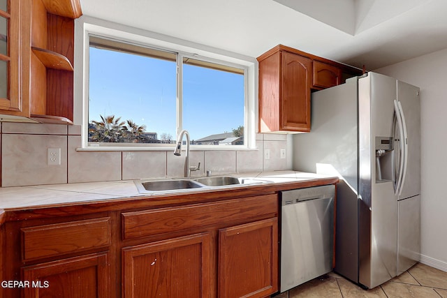 kitchen featuring sink, backsplash, stainless steel appliances, light tile patterned flooring, and tile countertops