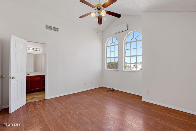 unfurnished bedroom featuring ensuite bath, vaulted ceiling, a textured ceiling, an AC wall unit, and hardwood / wood-style floors