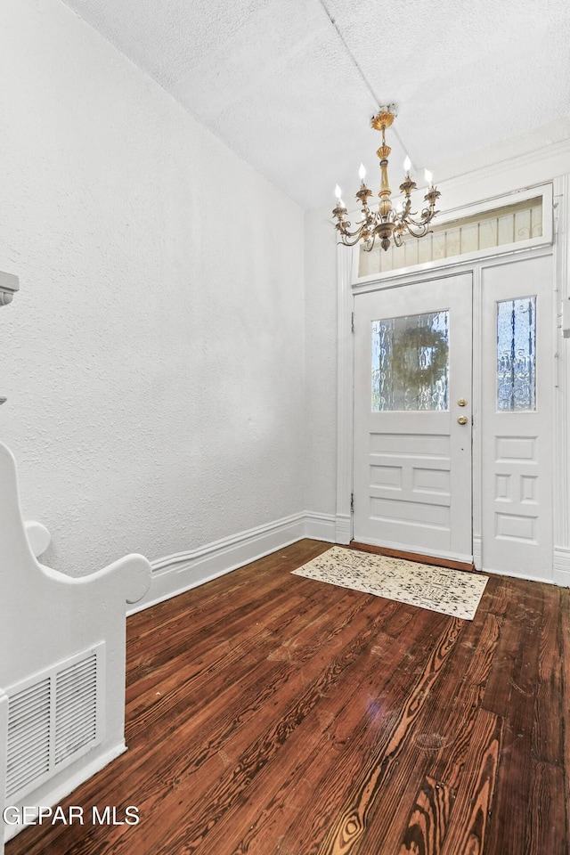 entrance foyer featuring dark wood-type flooring, a textured ceiling, and a notable chandelier