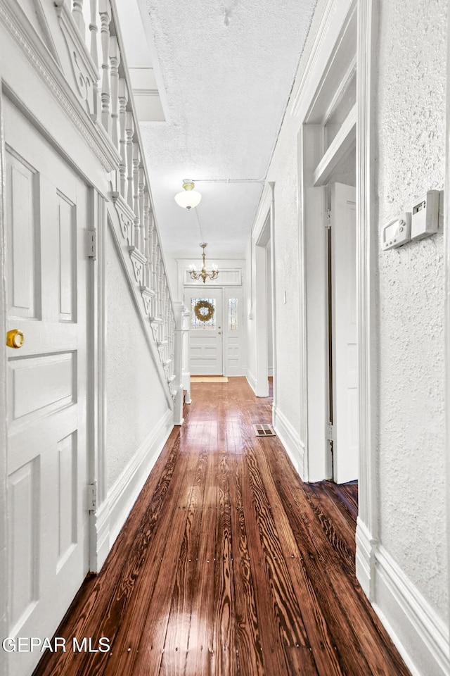 hallway with dark hardwood / wood-style floors, an inviting chandelier, and a textured ceiling