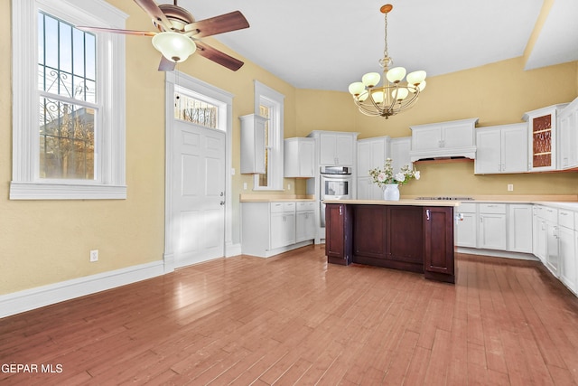 kitchen with pendant lighting, stovetop, white cabinets, stainless steel double oven, and light wood-type flooring