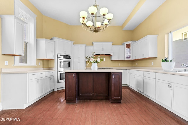 kitchen with white cabinetry, stainless steel double oven, decorative light fixtures, and sink