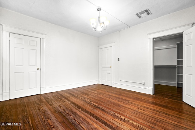 unfurnished bedroom featuring a walk in closet, dark wood-type flooring, a closet, and a chandelier