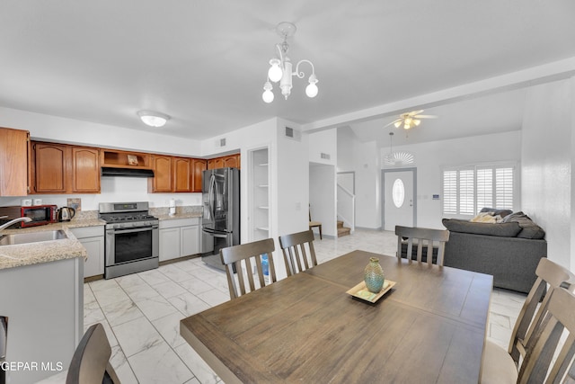 dining space with sink, ceiling fan with notable chandelier, and beam ceiling