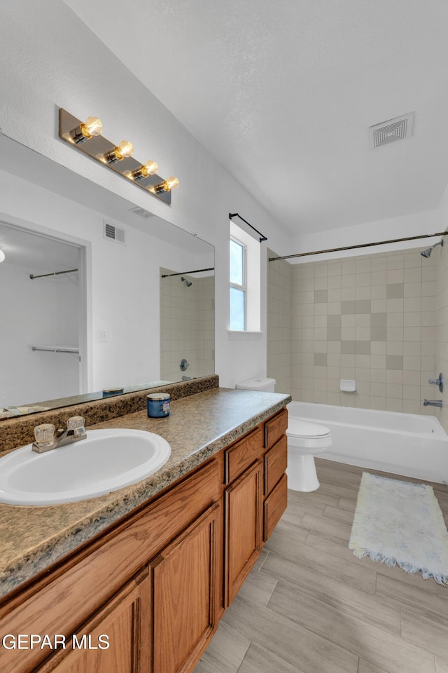 full bathroom featuring vanity, toilet, tiled shower / bath combo, and a textured ceiling