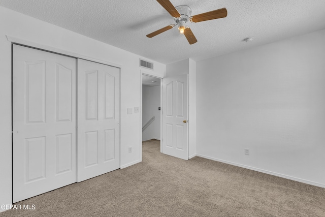 unfurnished bedroom with ceiling fan, light colored carpet, a textured ceiling, and a closet