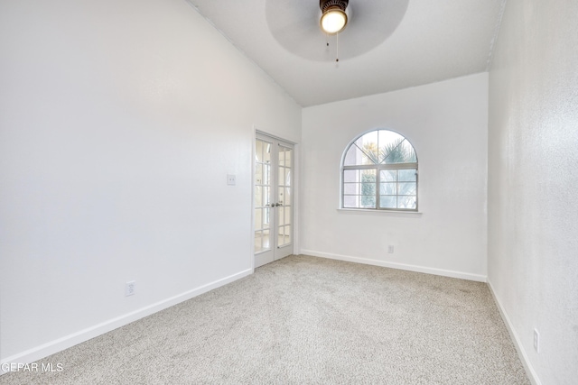 carpeted spare room featuring lofted ceiling, baseboards, a ceiling fan, and french doors