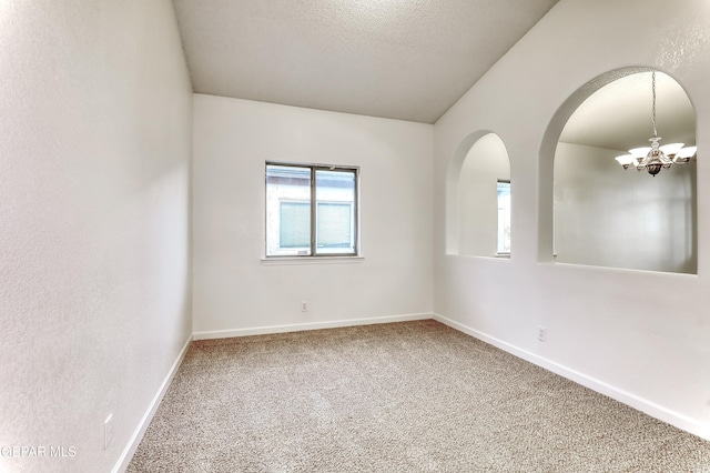 empty room featuring carpet, lofted ceiling, a textured ceiling, a chandelier, and baseboards