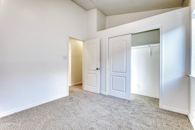 unfurnished bedroom featuring baseboards, vaulted ceiling, a closet, and light colored carpet