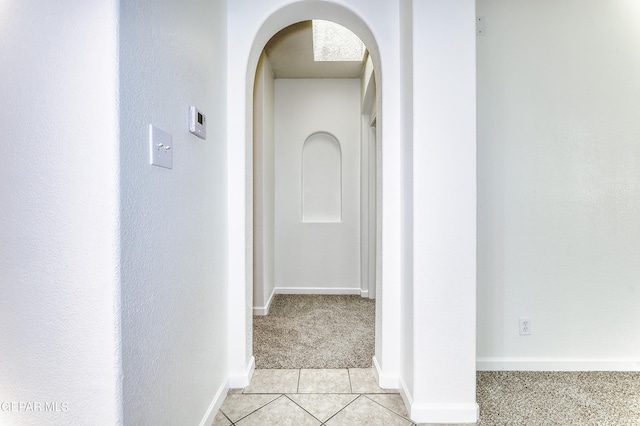 hall with arched walkways, light carpet, baseboards, and light tile patterned flooring