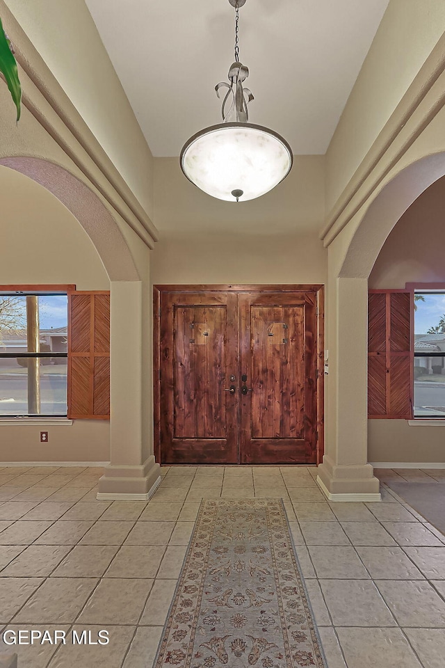 entrance foyer featuring ornate columns, a wealth of natural light, a towering ceiling, and light tile patterned floors