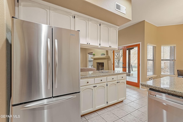 kitchen with light tile patterned floors, white cabinetry, stainless steel appliances, light stone counters, and french doors