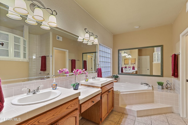 bathroom with tile patterned flooring, vanity, tasteful backsplash, tiled bath, and a chandelier