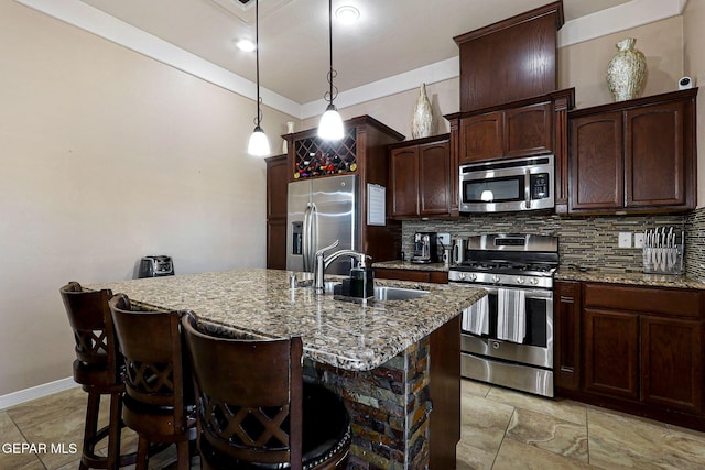 kitchen featuring sink, tasteful backsplash, appliances with stainless steel finishes, an island with sink, and light stone countertops