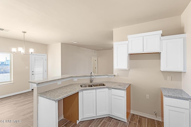 kitchen with sink, pendant lighting, white cabinets, and light stone counters