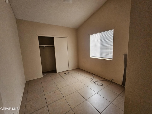 unfurnished bedroom with lofted ceiling, a textured ceiling, a closet, and light tile patterned floors