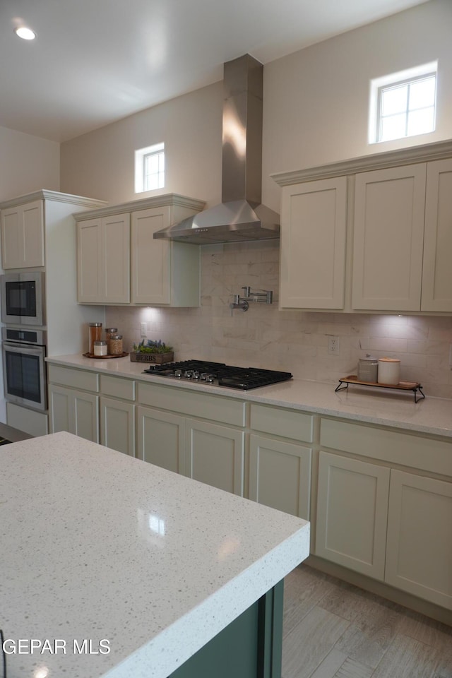 kitchen featuring tasteful backsplash, wall chimney range hood, light stone countertops, and appliances with stainless steel finishes