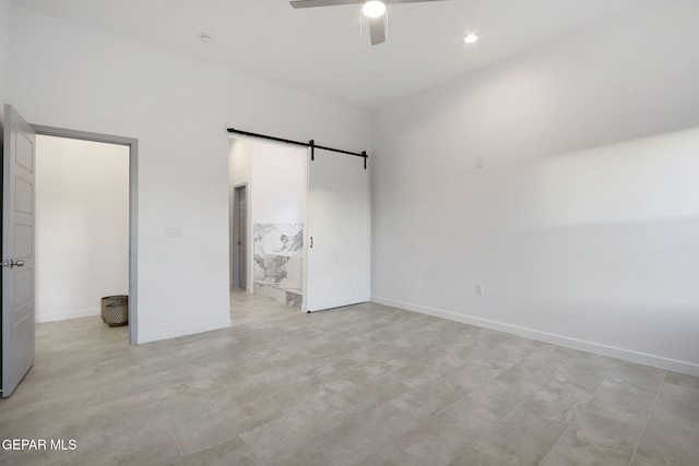 unfurnished bedroom featuring ceiling fan, a barn door, and baseboards