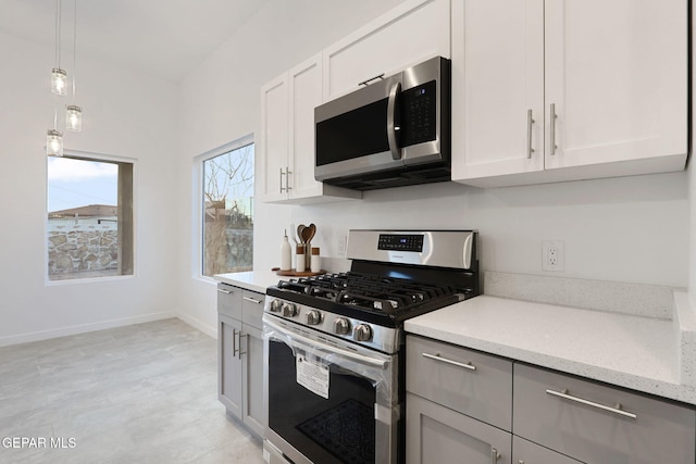 kitchen with decorative light fixtures, stainless steel appliances, gray cabinets, light stone countertops, and baseboards