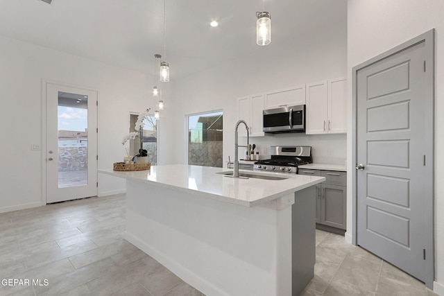 kitchen featuring light stone counters, a sink, appliances with stainless steel finishes, an island with sink, and decorative light fixtures