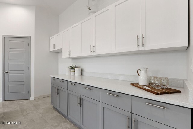 kitchen with baseboards, light stone counters, white cabinets, and gray cabinetry