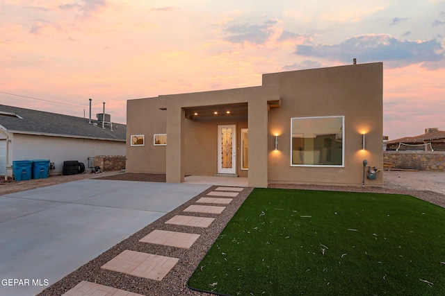 back of property at dusk with a yard and stucco siding