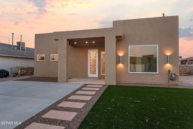 back of property at dusk featuring a lawn and stucco siding