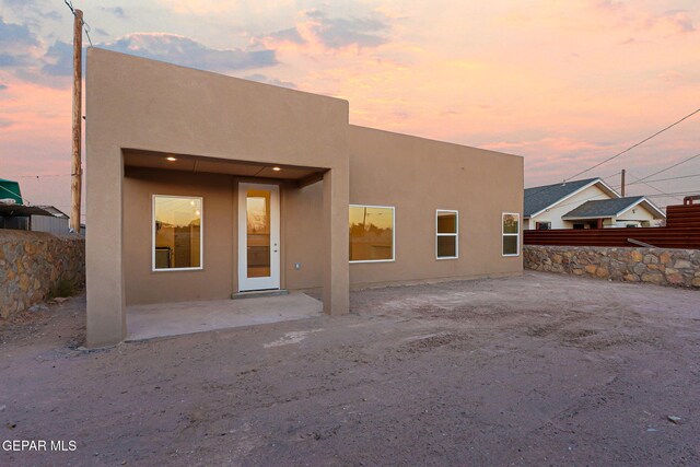 back of house at dusk with a patio, fence, and stucco siding