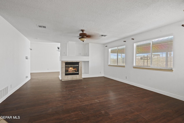 unfurnished living room featuring ceiling fan, dark hardwood / wood-style floors, a tiled fireplace, and a textured ceiling