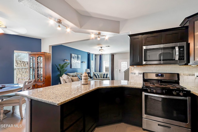 kitchen featuring light stone countertops, appliances with stainless steel finishes, kitchen peninsula, and decorative backsplash