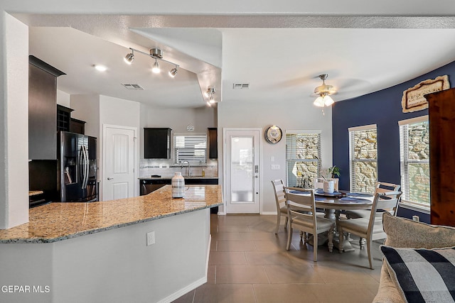 kitchen with visible vents, black fridge with ice dispenser, light stone countertops, tile patterned flooring, and a peninsula