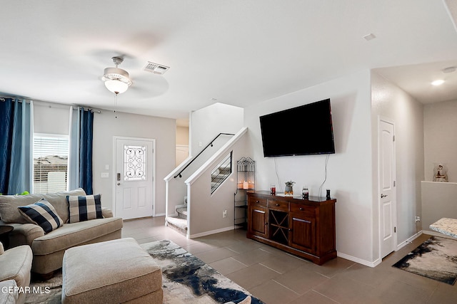 living room with light tile patterned floors, visible vents, baseboards, ceiling fan, and stairway