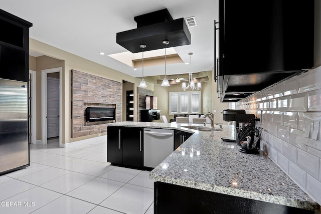 kitchen featuring decorative light fixtures, sink, light stone counters, a tray ceiling, and stainless steel appliances