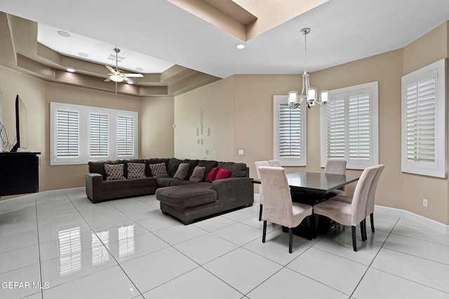 dining room with light tile patterned floors, ceiling fan with notable chandelier, and a raised ceiling