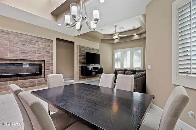 dining room featuring a fireplace, a raised ceiling, and ceiling fan with notable chandelier